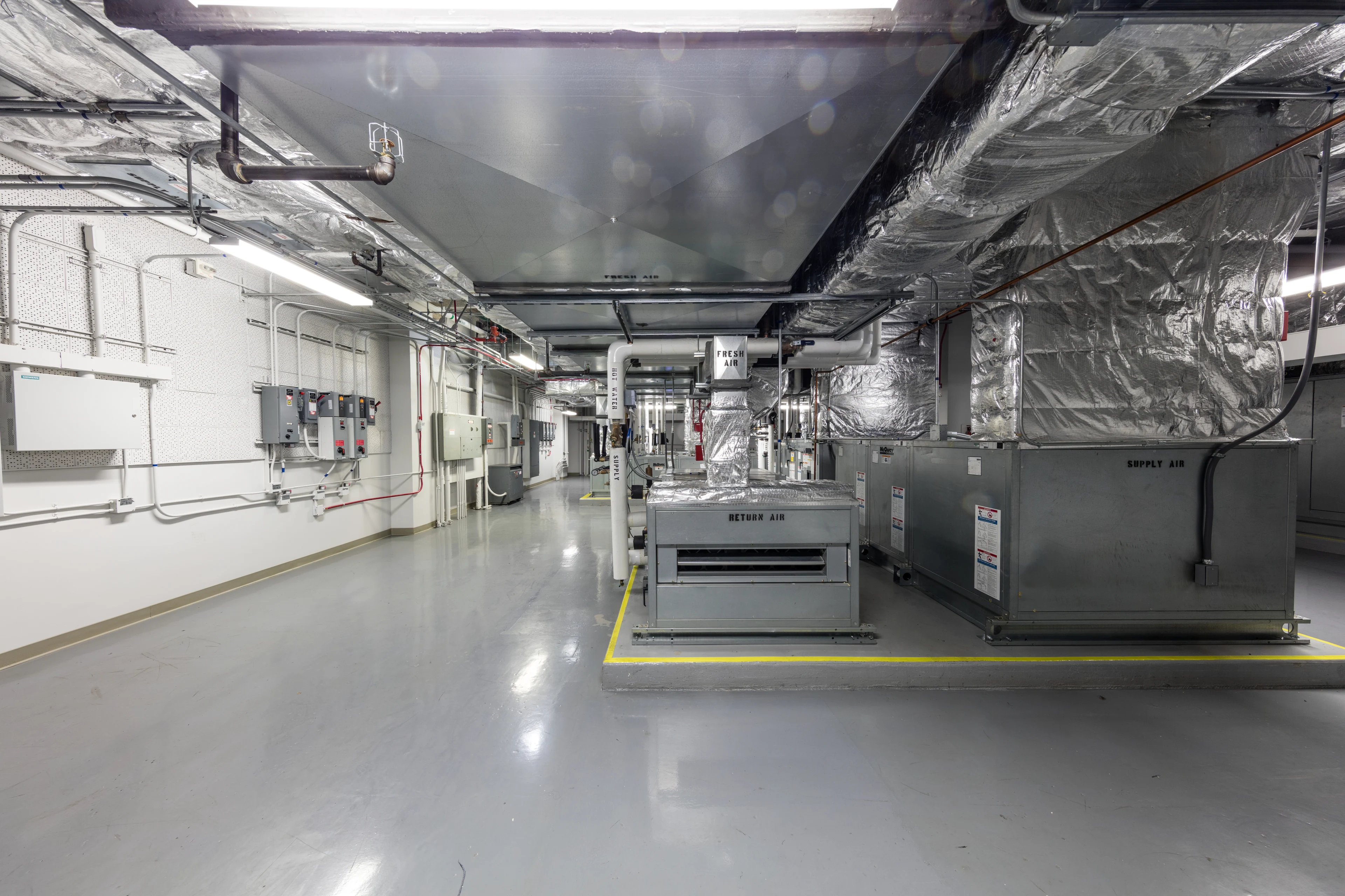 Sala técnica de climatização com equipamentos de insuflação e retorno de ar conectados a grandes dutos isolados; fotografia de referência