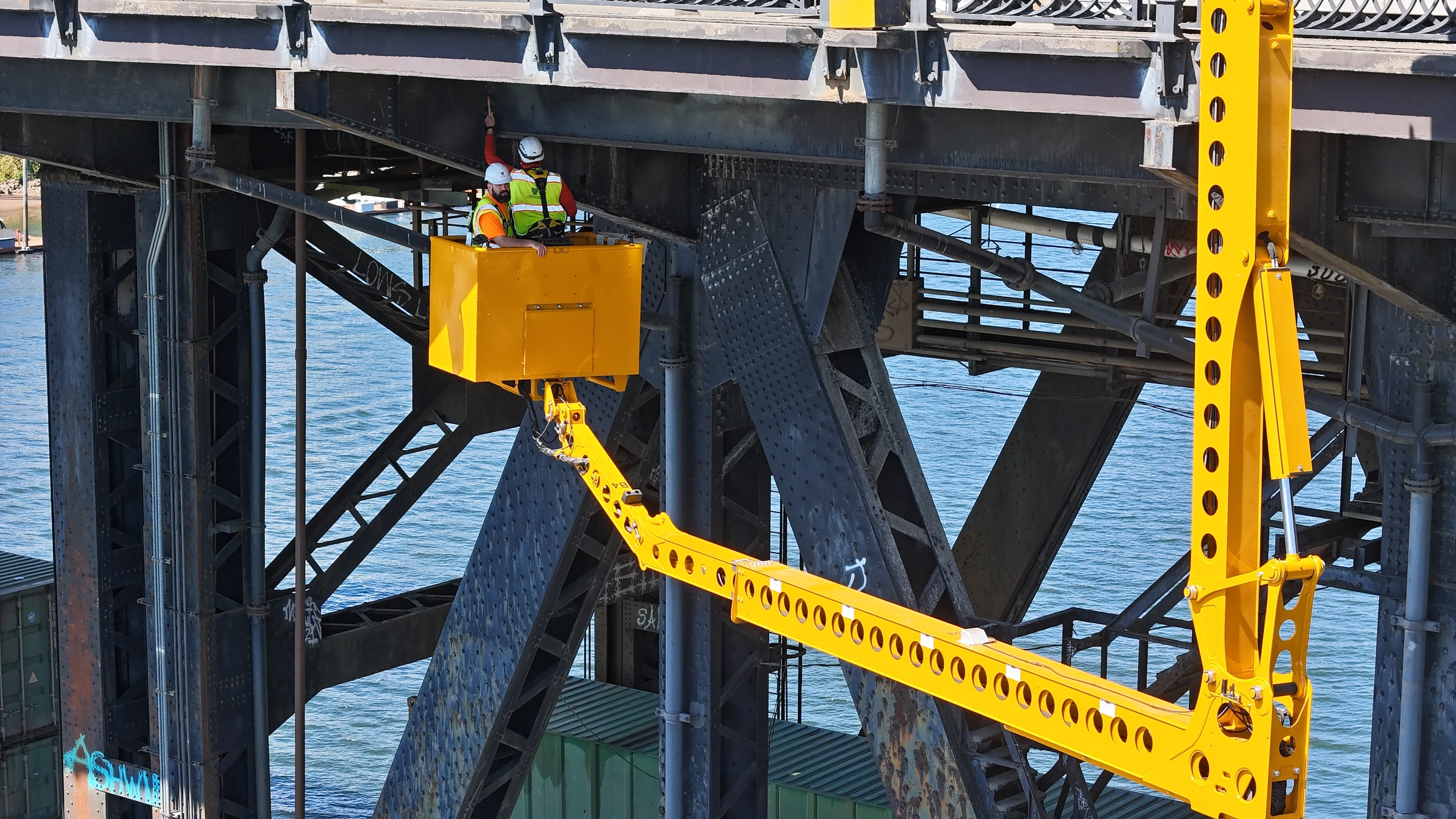 Equipe em plataforma de acesso inspeciona elementos de aço sob o tabuleiro de uma ponte